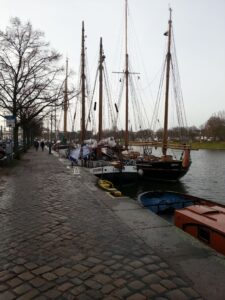 Billedet viser kanalen der går rundt om Lübeck. Billedet viser desuden nogle gamle træskibe ligge til kajs.